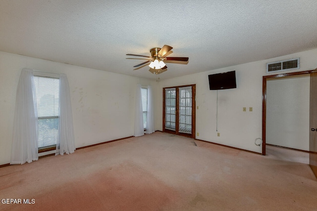 empty room with a textured ceiling, french doors, light colored carpet, and ceiling fan