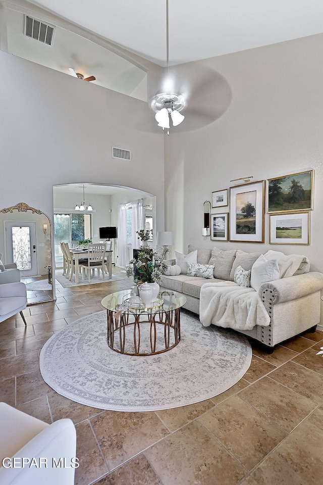 living room featuring ceiling fan with notable chandelier and a high ceiling