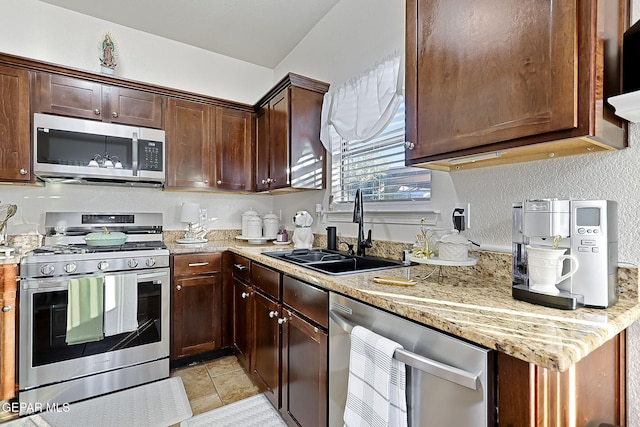 kitchen with stainless steel appliances, light stone countertops, dark brown cabinets, and sink