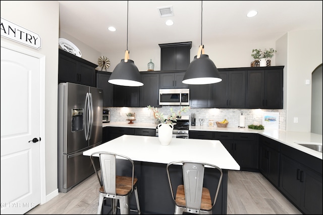 kitchen with backsplash, stainless steel appliances, hanging light fixtures, and light hardwood / wood-style flooring