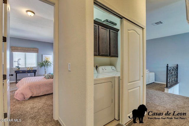 laundry area featuring washer and clothes dryer, light carpet, and cabinets