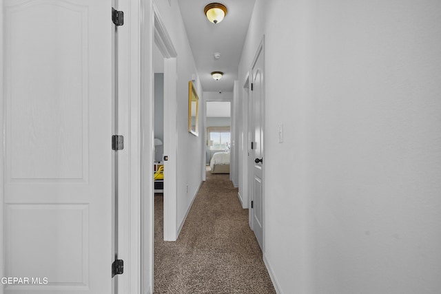 corridor featuring baseboards and dark carpet