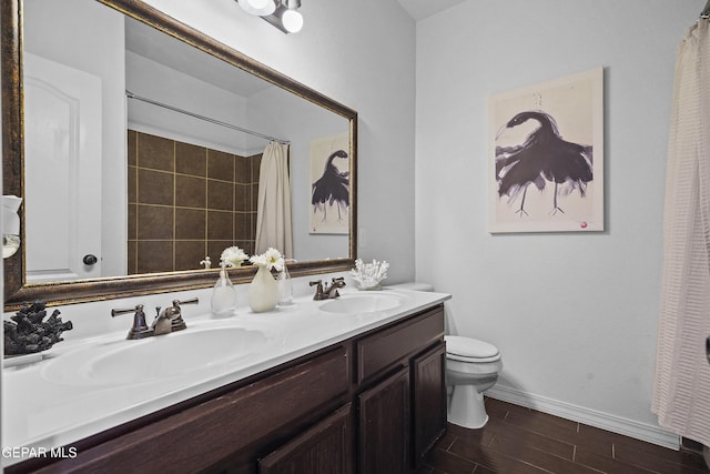 bathroom with a sink, double vanity, toilet, and baseboards