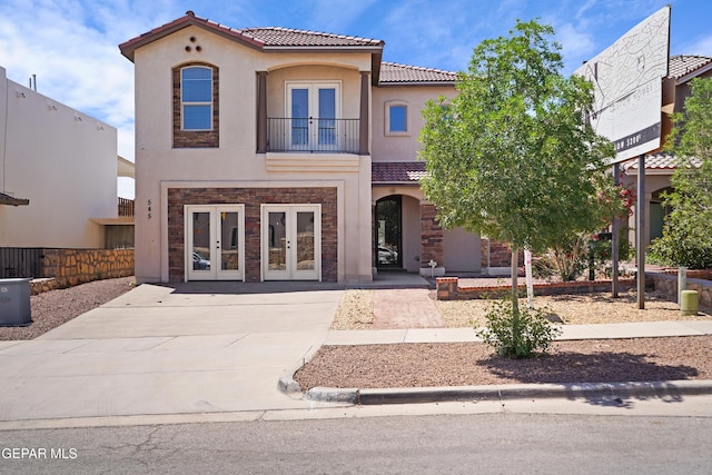 mediterranean / spanish-style house with a balcony, french doors, stucco siding, a tile roof, and stone siding