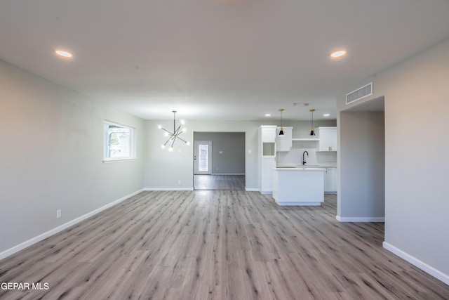 unfurnished living room with light wood-type flooring and an inviting chandelier