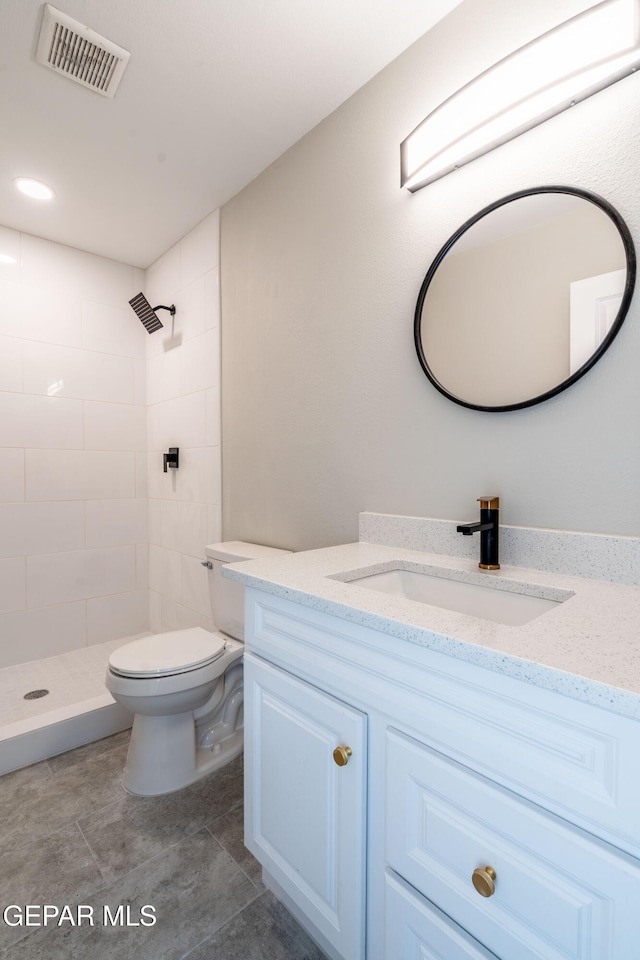 bathroom featuring tile patterned flooring, vanity, toilet, and a tile shower