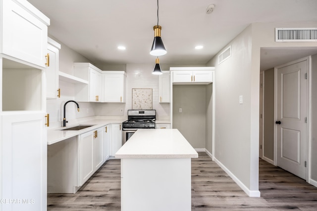 kitchen featuring stainless steel gas range, sink, a center island, white cabinets, and pendant lighting