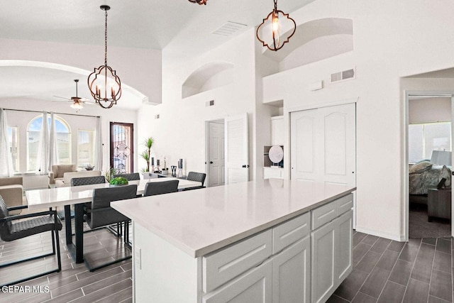 kitchen featuring white cabinetry, ceiling fan with notable chandelier, decorative light fixtures, high vaulted ceiling, and a center island