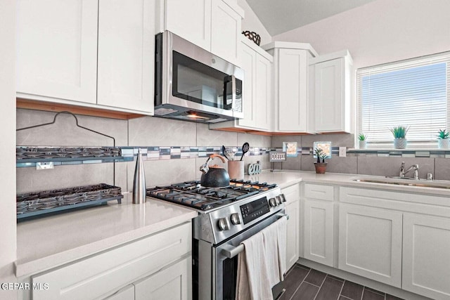 kitchen with vaulted ceiling, sink, backsplash, white cabinetry, and appliances with stainless steel finishes