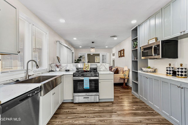 kitchen with kitchen peninsula, dark hardwood / wood-style flooring, stainless steel appliances, sink, and hanging light fixtures