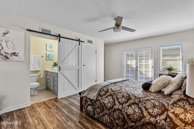 bedroom featuring ensuite bath, ceiling fan, french doors, a barn door, and hardwood / wood-style floors