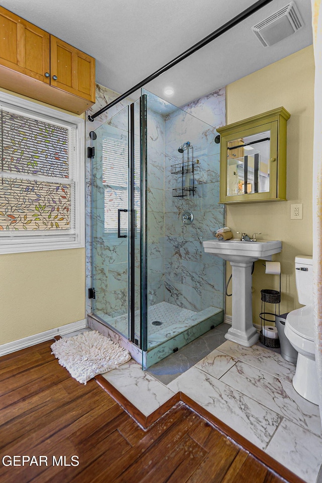 bathroom featuring toilet, a shower with shower door, and sink