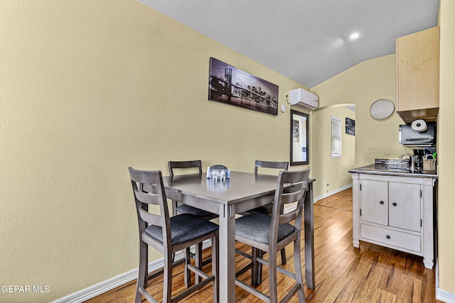 dining room featuring lofted ceiling, light hardwood / wood-style flooring, a wall mounted air conditioner, and sink