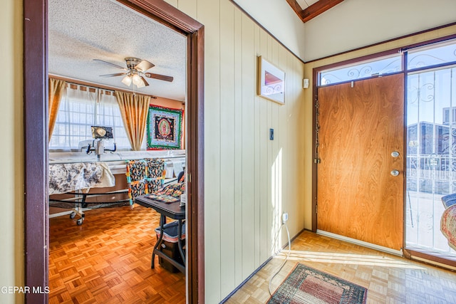 foyer featuring a textured ceiling, wooden walls, parquet flooring, and ceiling fan