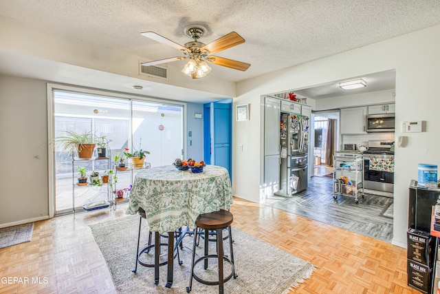 dining area featuring ceiling fan, parquet flooring, a healthy amount of sunlight, and a textured ceiling