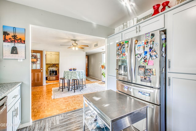 kitchen featuring light parquet floors, appliances with stainless steel finishes, ceiling fan, and white cabinets