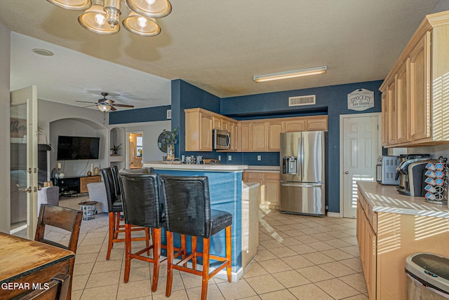 kitchen featuring a breakfast bar, appliances with stainless steel finishes, light brown cabinets, ceiling fan with notable chandelier, and light tile patterned floors