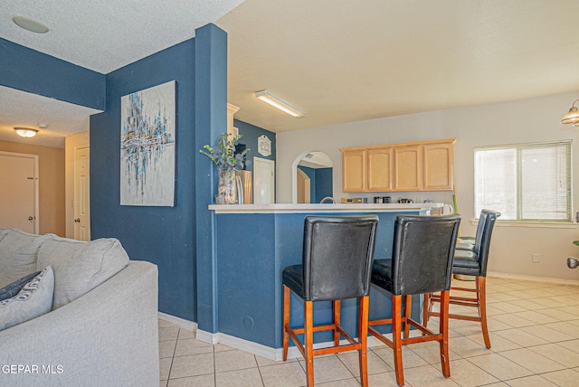 kitchen featuring stainless steel refrigerator, light brown cabinets, a kitchen breakfast bar, a textured ceiling, and light tile patterned floors