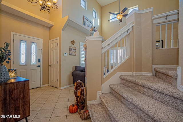 foyer with ceiling fan with notable chandelier, plenty of natural light, light tile patterned floors, and a high ceiling