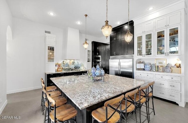 kitchen with light stone counters, a center island, built in appliances, hanging light fixtures, and a breakfast bar area