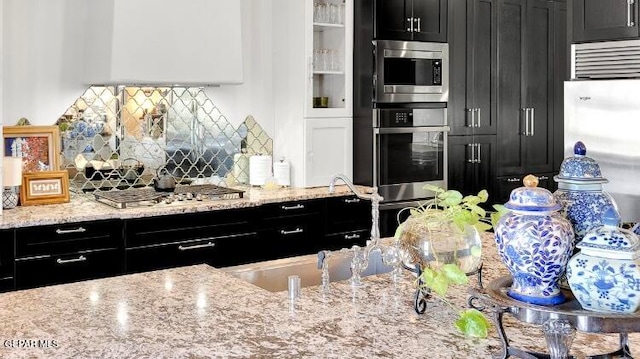 kitchen featuring stainless steel appliances, light stone countertops, white cabinets, and backsplash