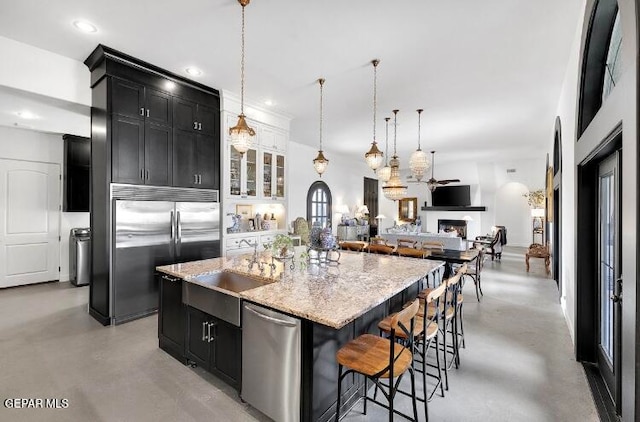 kitchen with a center island with sink, appliances with stainless steel finishes, light stone countertops, a breakfast bar area, and decorative light fixtures