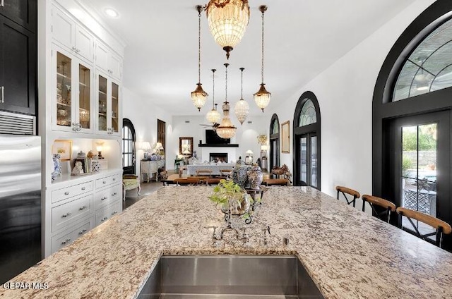 kitchen with pendant lighting, stainless steel built in fridge, white cabinetry, and light stone countertops