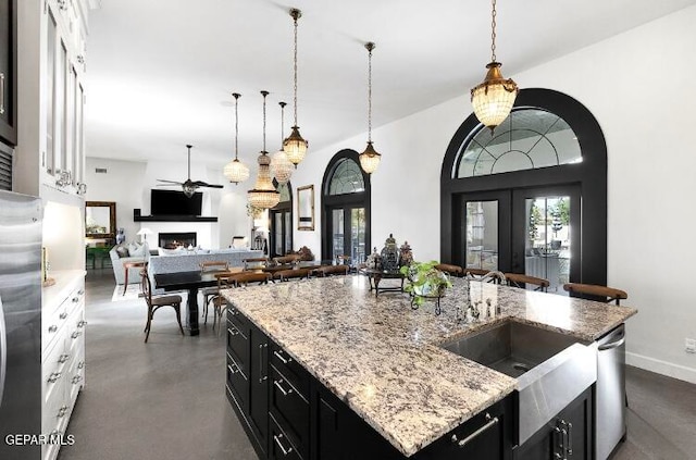 kitchen featuring white cabinetry, appliances with stainless steel finishes, light stone countertops, an island with sink, and ceiling fan