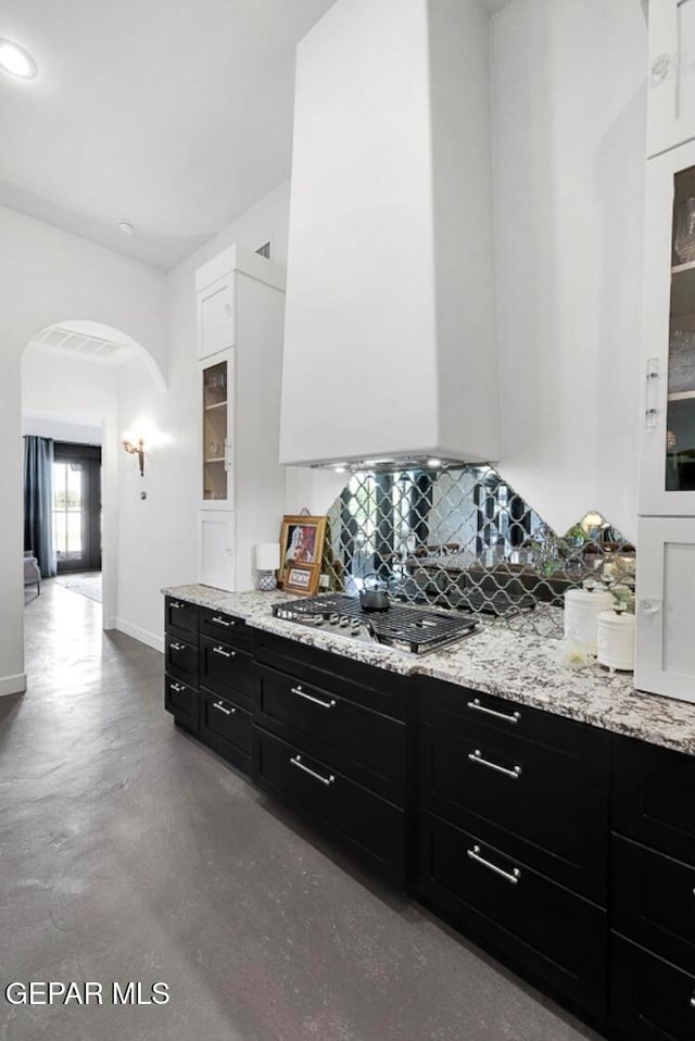 kitchen with white cabinetry, stainless steel gas stovetop, backsplash, and concrete floors