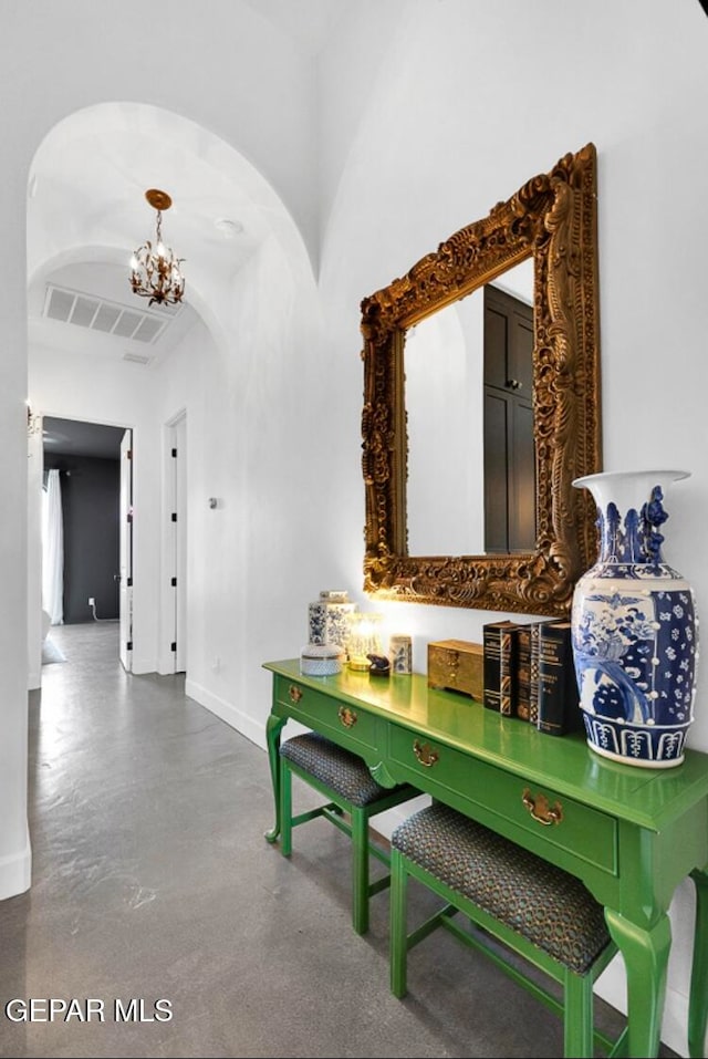 hallway featuring concrete flooring and a chandelier