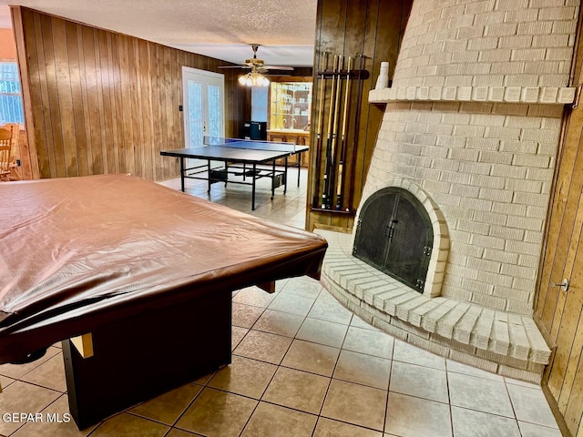 playroom with wood walls, tile patterned flooring, ceiling fan, and a fireplace