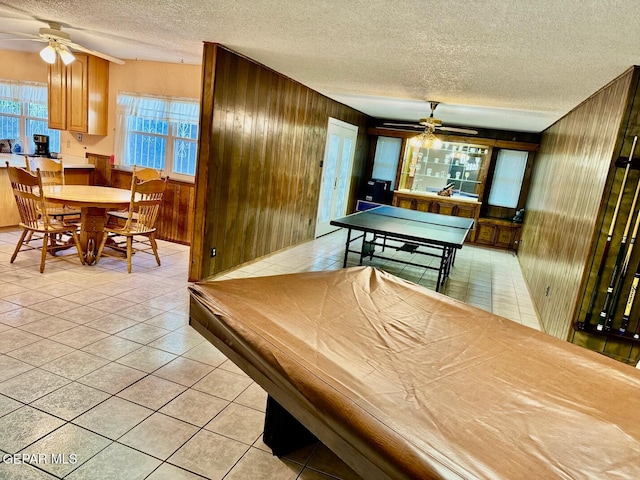 rec room with wood walls, a textured ceiling, and light tile patterned floors