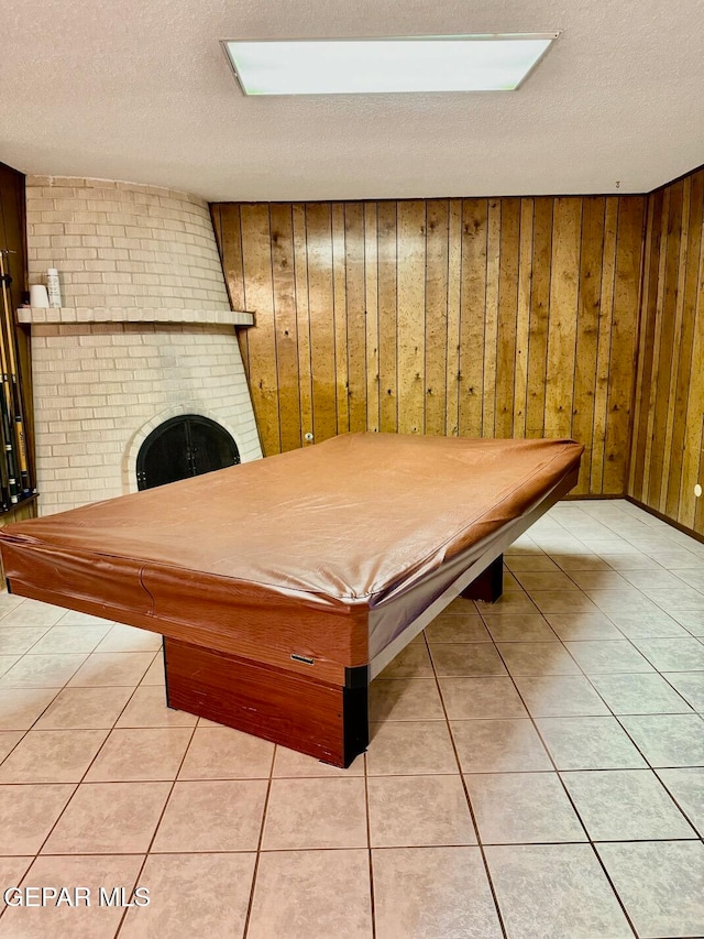 recreation room with wood walls, a textured ceiling, light tile patterned floors, and a fireplace