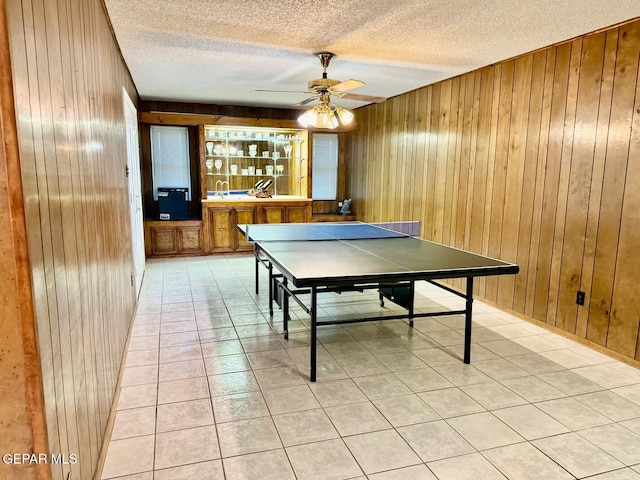 recreation room with a textured ceiling, wood walls, and ceiling fan
