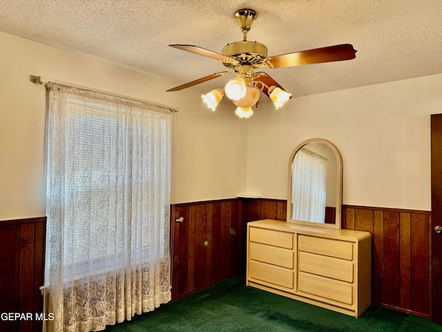 bedroom with a textured ceiling, multiple windows, dark colored carpet, and ceiling fan
