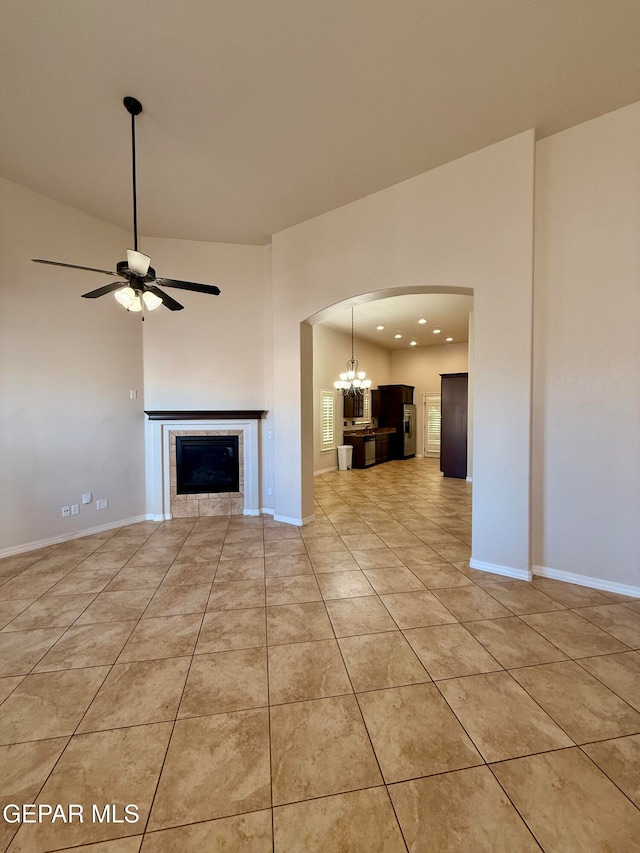 unfurnished living room featuring ceiling fan with notable chandelier, light tile patterned floors, and a tile fireplace