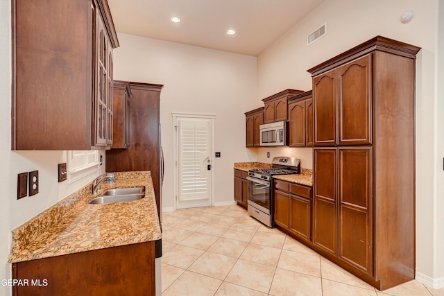 kitchen with light tile patterned flooring, sink, light stone countertops, and stainless steel appliances