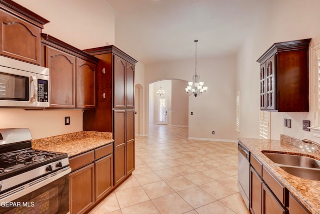 kitchen with sink, hanging light fixtures, appliances with stainless steel finishes, light tile patterned flooring, and light stone counters