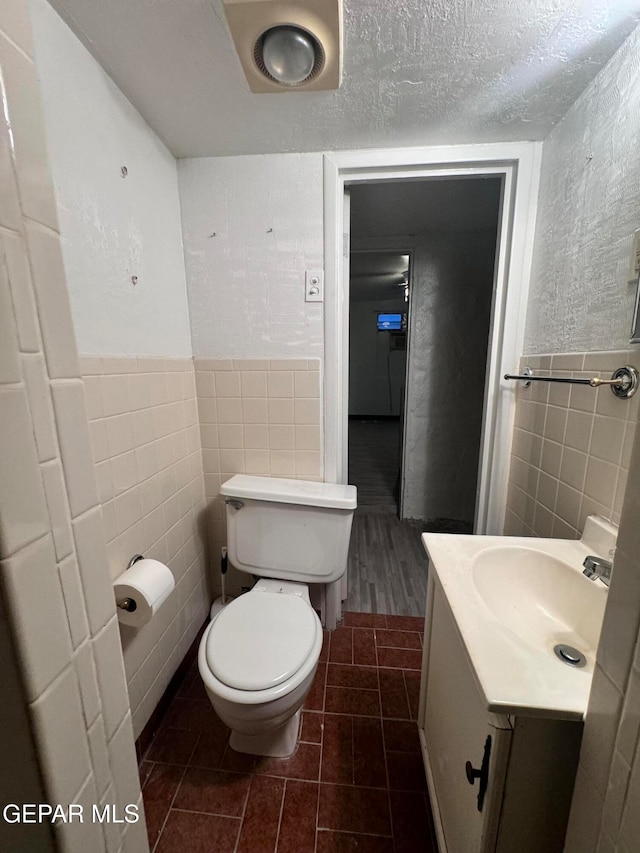 bathroom with toilet, tile walls, tile patterned flooring, a textured ceiling, and vanity