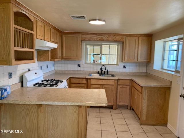 kitchen with kitchen peninsula, decorative backsplash, white gas stove, light tile patterned flooring, and sink