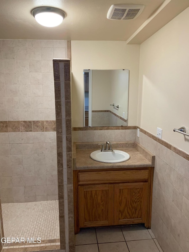 bathroom with tile walls, a shower, tile patterned floors, and vanity