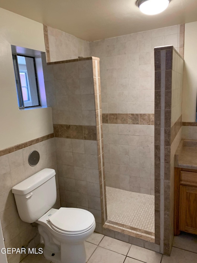 bathroom with toilet, tiled shower, tile patterned flooring, tile walls, and vanity