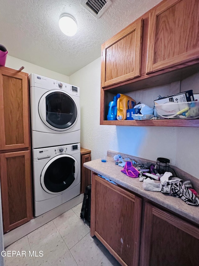 laundry area featuring cabinets, stacked washer and clothes dryer, and a textured ceiling