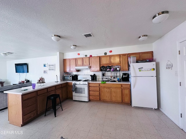 kitchen featuring white appliances, a textured ceiling, sink, and kitchen peninsula