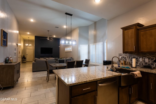 kitchen featuring light stone counters, pendant lighting, stainless steel dishwasher, kitchen peninsula, and ceiling fan with notable chandelier