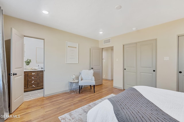 bedroom with ensuite bath, light wood-type flooring, and a closet