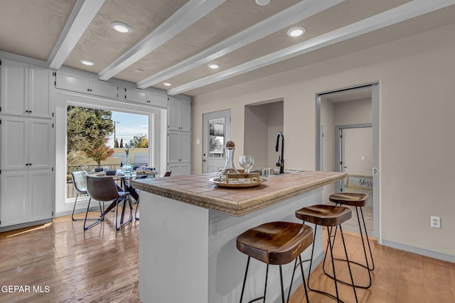 kitchen with sink, light hardwood / wood-style flooring, beamed ceiling, white cabinets, and a kitchen island