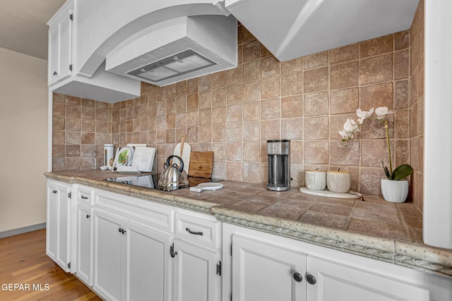 kitchen featuring decorative backsplash, white cabinetry, extractor fan, and light hardwood / wood-style flooring