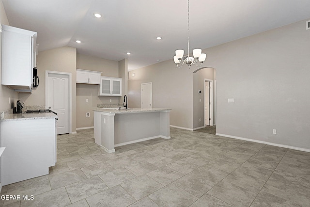 kitchen featuring light stone counters, pendant lighting, vaulted ceiling, an island with sink, and white cabinets