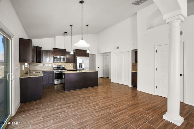 kitchen with stainless steel appliances, decorative light fixtures, high vaulted ceiling, a center island, and dark hardwood / wood-style flooring